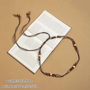 Détail d'une chaîne de taille bohème avec perles en bois et pompons sur un livre ouvert