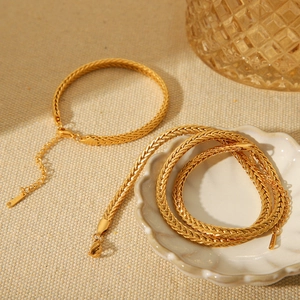 Elegant 18K gold plated braided chain necklace and bracelet set on a textured fabric