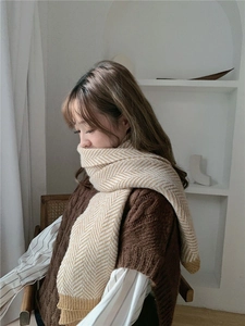 Dettaglio della sciarpa in maglia a spina di pesce beige e bianca su una modella