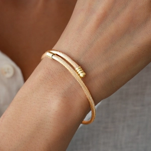 Close-up of golden twisted cable cuff bracelet with textured cylindrical metal ends