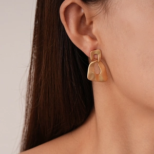 Detail of matte gold irregular geometric earrings showing texture on female model