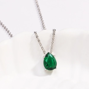 Macro view of teardrop emerald pendant in four-prong silver setting on link chain