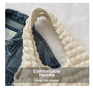 Détail de la poignée du sac à main texturé crème sur un fond en jean bleu denim