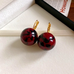 Detailed macro view of red and black leopard pattern acrylic ball earrings with gold clasp