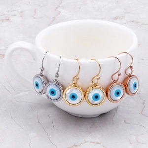 Three pairs of Evil Eye earrings in silver, gold, and rose gold on a white ceramic cup
