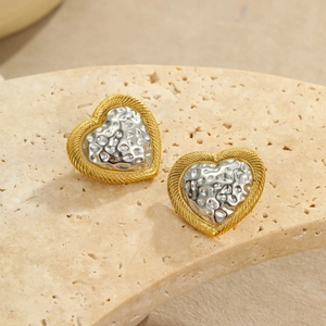 Macro shot of two-tone heart stud earrings with hammered silver texture on beige stone