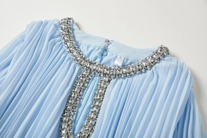 Détails de la robe plissée bleu clair avec broderie perlée et strass sur l'encolure