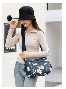 Detail of blue floral print crossbody bag with multiple zippers and wide strap on model