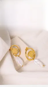 Close-up of baroque pearl earrings with irregular textured gold circles on a stone tray