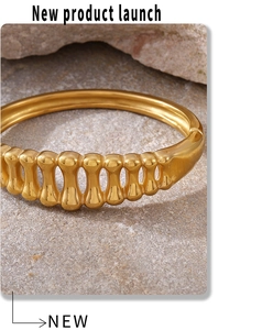 Macro detail of gold fishbone hollow cuff bracelet on a natural stone surface
