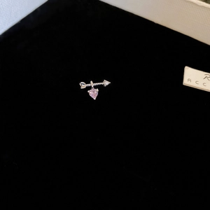 Macro shot of a silver arrow stud earring featuring a delicate pink heart-shaped zircon