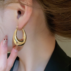Close-up of chunky gold-plated C-shaped hoop earrings with a sleek mirrored finish
