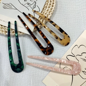 Detail of five acetate U-shaped hair pins in tortoise and marble patterns on a linen cloth