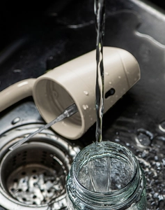 Washable oil dispenser head with waterproof design being rinsed under a water faucet