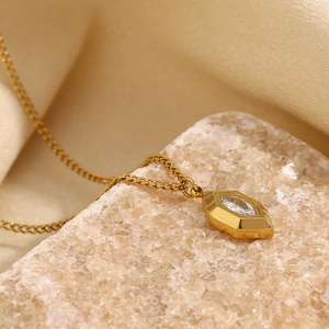 Close-up of gold plated rhombus pendant with white crystal on natural stone