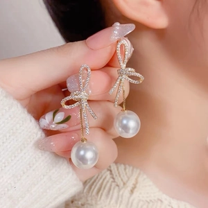 Elegant gold bow earrings with pavé crystals and white pearl drops on a warm background