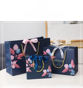 Three deep blue floral paper gift bags in various sizes with elegant gold rope handles
