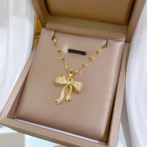 Detail view of gold bow pendant with sparkling zircon in a beige jewelry box