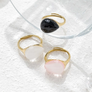 Three gold water-drop moonstone rings in black, white, and pink on a white textured background