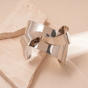 Macro detail of high-polish silver geometric knotted cuff bracelet on a stone surface