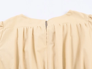 Detail of round neckline with pleated shoulders and back button on beige cotton top