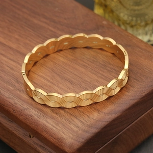 Detailed view of a gold-toned bangle with 3D wave texture on a vintage wood box