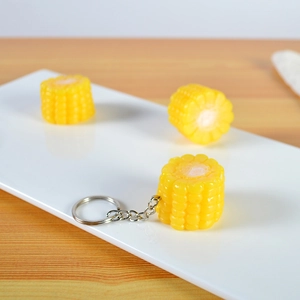 Realistic yellow corn keychain pendant with silver metal ring on a wooden surface