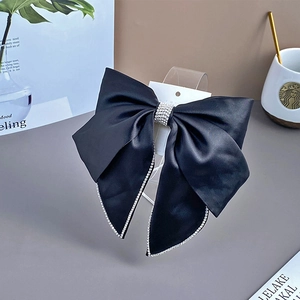 Macro detail of black satin bow hair clip featuring luxury rhinestone trim and diamond center