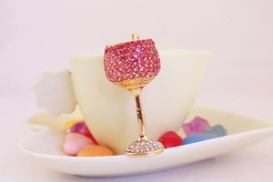 Detail of gold goblet keychain with pink and white rhinestones hanging on a white ceramic cup