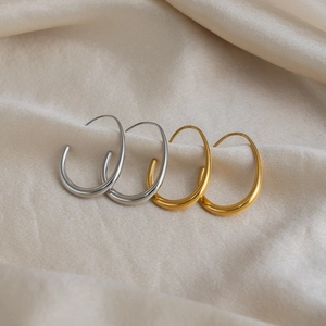 Minimalist U-shaped hoop earrings in 18K gold and silver plating on silk background