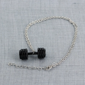 Close-up of a silver chain necklace featuring a black dumbbell pendant on gray linen fabric