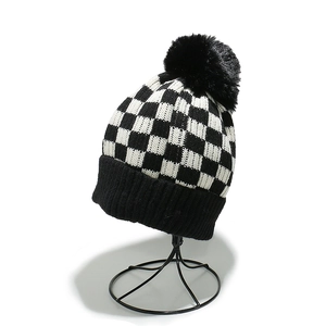 Women's black and white checkered knit beanie featuring a fluffy black faux fur pompom