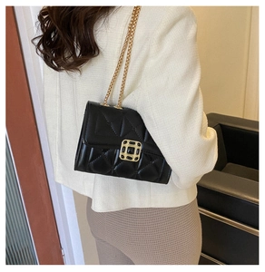 Detail of black quilted leather shoulder bag with gold chain and metal buckle on a model