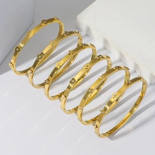 Dettaglio di sei bracciali dorati con motivi floreali e gemme chiare su sfondo bianco