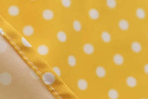 Macro shot of white polka dots on yellow fabric showing precise stitching on the dress hem