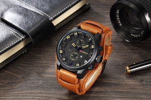 Detail of quartz watch with brown leather strap and black dial on dark wood surface