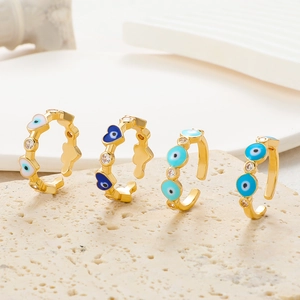 Close-up of four gold evil eye rings with colorful zircon on a stone surface