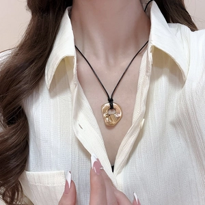 Close-up of a gold irregular geometric pendant on a black cord necklace worn by a model