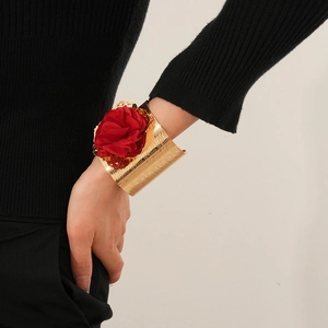 Gros plan d'un large bracelet manchette doré texturé avec une grande fleur en tissu rouge