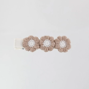 Close-up of three knitted beige flower petals on a white ribbon-wrapped hair clip