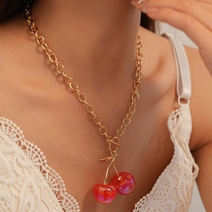 Close-up of golden chain necklace featuring red resin cherry charms and OT toggle clasp