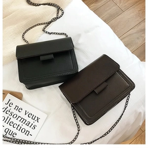 Macro shot of black and brown chain crossbody bags on a white textured fabric background