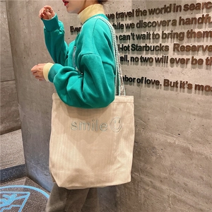 Detail of cream canvas tote featuring blue smile embroidery and green bead shoulder strap