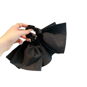 Oversized black fabric bow scrunchie with matte texture shown in hand on white background