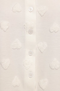 Détail du haut blanc montrant la broderie cœur floquée et le bouton en résine en gros plan