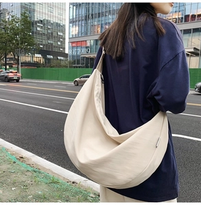 Outdoor shot of a cream-white large capacity crescent crossbody bag with black zipper