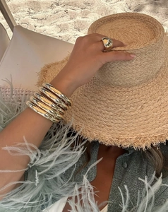 Lifestyle-Foto mit polierten goldenen Armreifen und Ring auf einem sommerlichen Strohhut