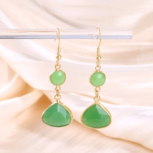 Detailed close-up of emerald green teardrop crystal earrings on a cream satin background