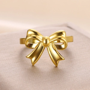 Elegant gold bow ring with matte finish and center sphere on a warm beige background