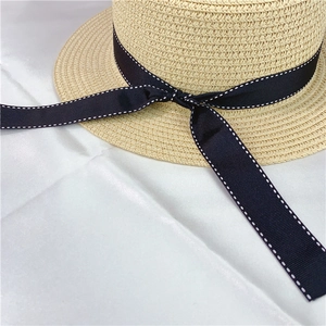 Detail of light beige straw boater hat with black bow ribbon and white dotted trim